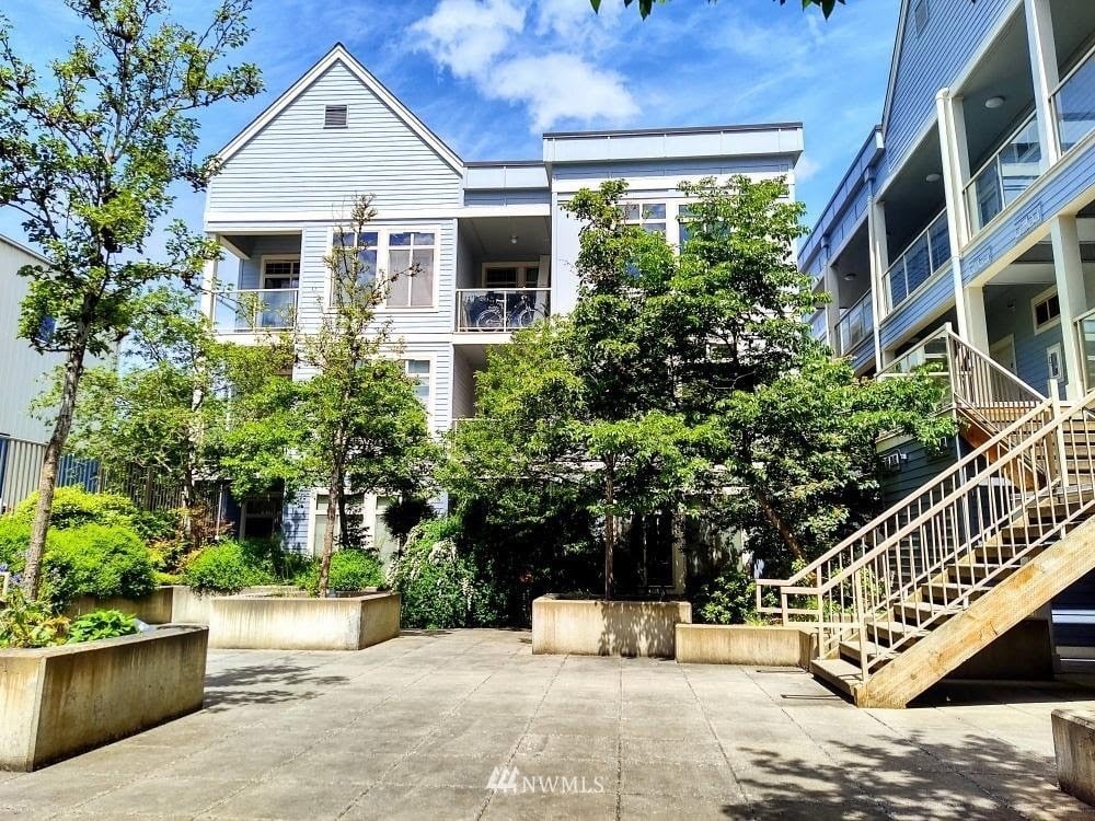 A three-story condo building behind a landscaped courtyard with trees and concrete planters
